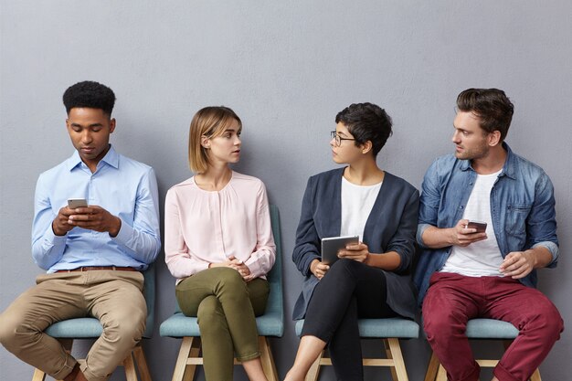 Jovens empreendedores talentosos discutem, sentam em cadeiras na fila