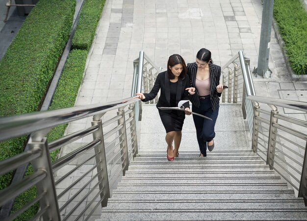 Jovens empresárias asiáticas com documentário andando nas escadas.