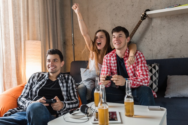 Jovens felizes jogando videogame, se divertindo, festa de amigos em casa, companhia hipster juntos, dois homens uma mulher, sorrindo, positivo, relaxado, emocional, rindo, competição