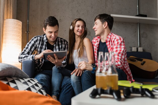 Jovens felizes usando tablet, alunos aprendendo, se divertindo, festa de amigos em casa, companhia hipster juntos, dois homens uma mulher, sorrindo, positivo, educação online, ouvindo música