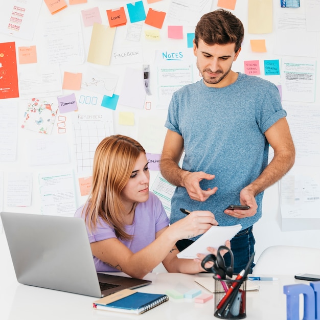 Jovens funcionários analisando escritos no caderno perto do local de trabalho