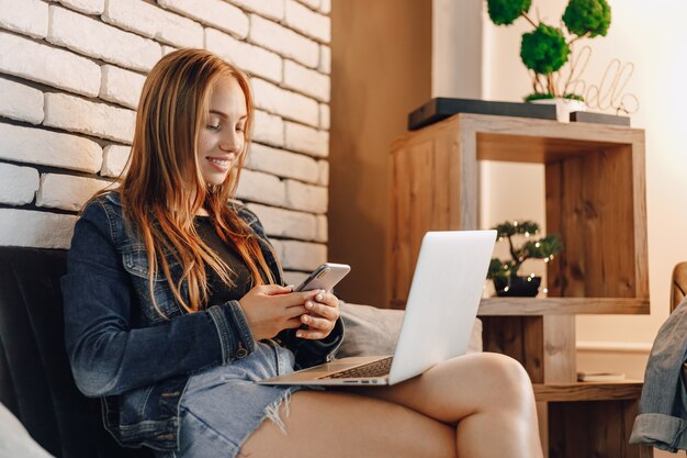 Jovens garotas atraentes em uma loja de eletrônicos em uma área de estar no sofá com laptops e telefones