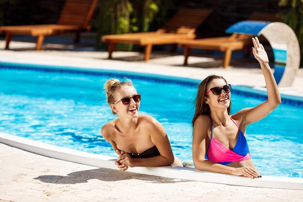 Jovens garotas bonitas sorrindo, cumprimentando, relaxando na piscina.