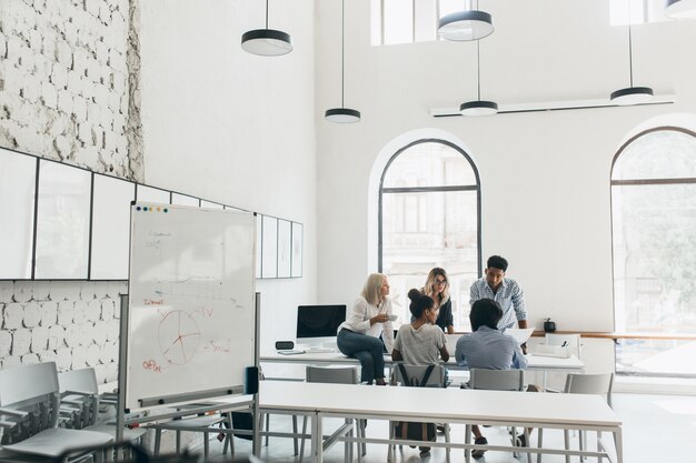 Jovens gerentes e CEO passando um tempo na sala de conferências pela manhã. Retrato interno da equipe de profissionais de marketing discutindo novos objetivos em um grande escritório moderno.