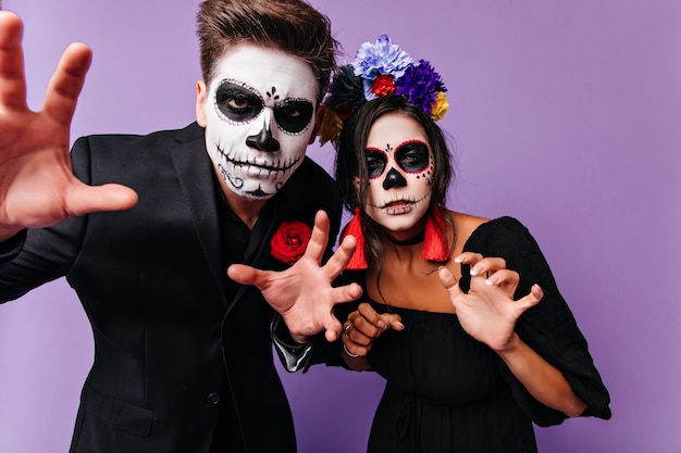 Jovens morenos fazendo caretas durante a sessão de fotos de halloween. Amigos refinados se divertindo na festa em fantasias de zumbi.