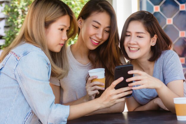 Jovens mulheres asiáticas alegres que sentam-se no café que bebe o café com amigos e que falam junto