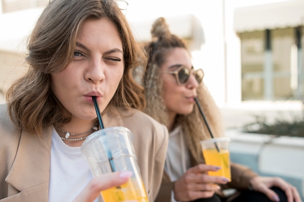Jovens mulheres bonitas que bebem suco de laranja