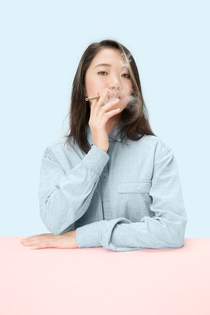 Jovens mulheres coreanas fumando charuto enquanto está sentado à mesa no estúdio.