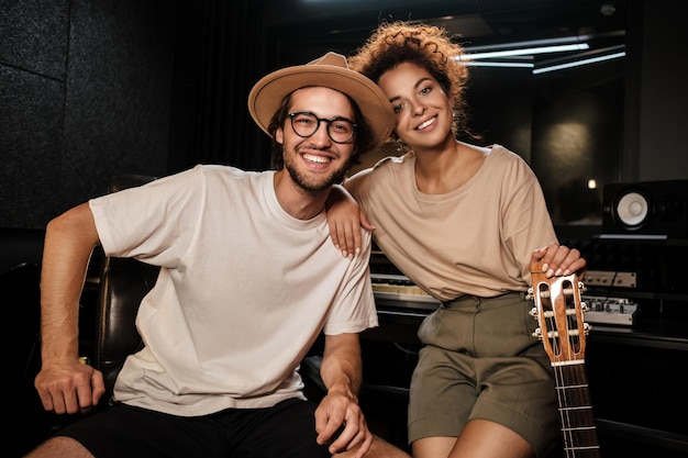 Foto grátis jovens músicos elegantes olhando alegremente na câmera trabalhando juntos em nova música no estúdio de gravação de som moderno. produção musical