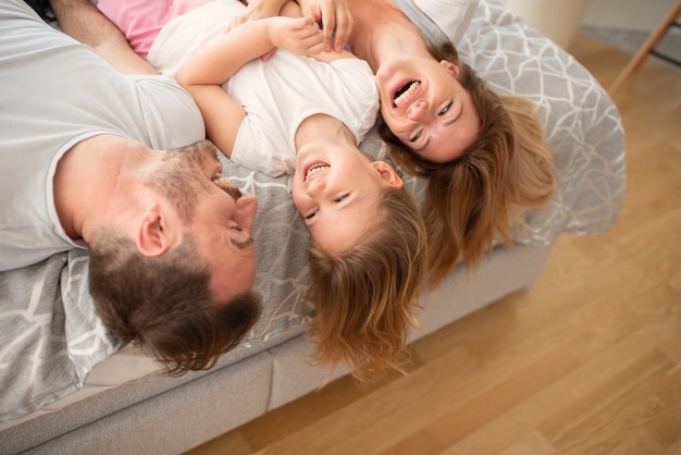 Jovens pais caucasianos felizes rindo enquanto deitam na cama com a filha.