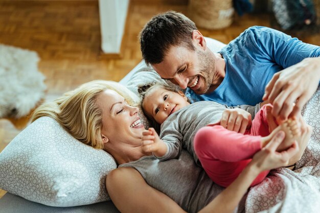 Jovens pais felizes se divertindo com sua filha pequena enquanto relaxam na cama