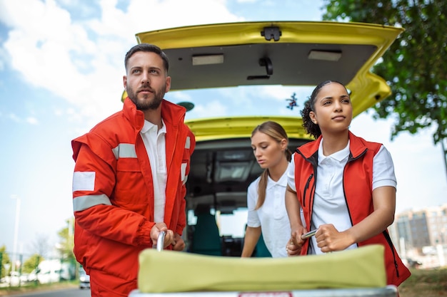 Jovens paramédicos movendo maca de ambulância do carro com pressa Paramédicos de uniforme tirando maca do carro da ambulância
