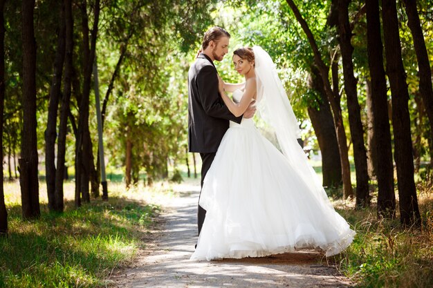 Jovens recém-casados elegantes lindos sorrindo, posando, abraçando no parque.