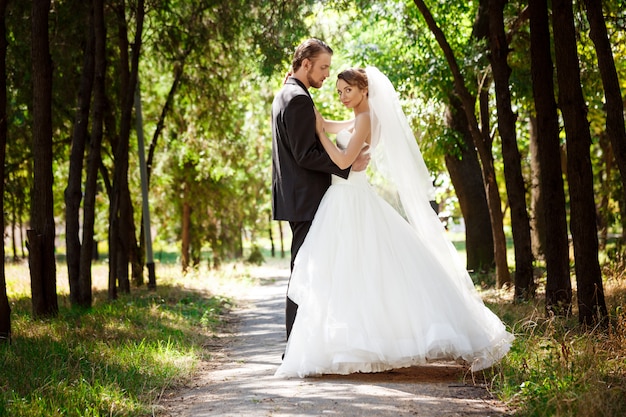 Jovens recém-casados elegantes lindos sorrindo, posando, abraçando no parque.