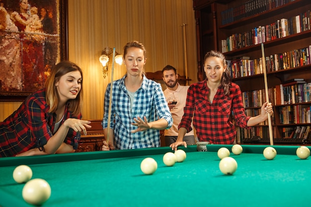 Jovens sorrindo, homens e mulheres jogando bilhar no escritório ou em casa, depois do trabalho. Colegas de trabalho envolvidos em atividades recreativas. Amizade, atividade de lazer, conceito de jogo.