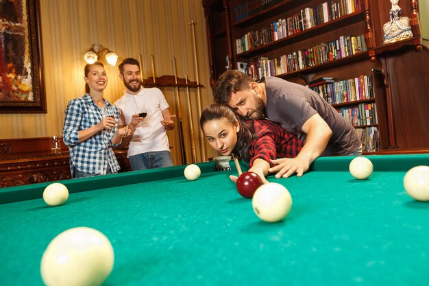 Jovens sorrindo, homens e mulheres jogando bilhar no escritório ou em casa, depois do trabalho. Colegas de trabalho envolvidos em atividades recreativas