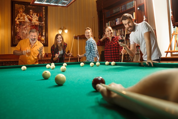 Foto grátis jovens sorrindo, homens e mulheres jogando bilhar no escritório ou em casa, depois do trabalho.