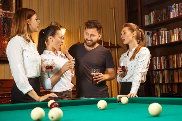 Jovens sorrindo, homens e mulheres jogando bilhar no escritório ou em casa, depois do trabalho.