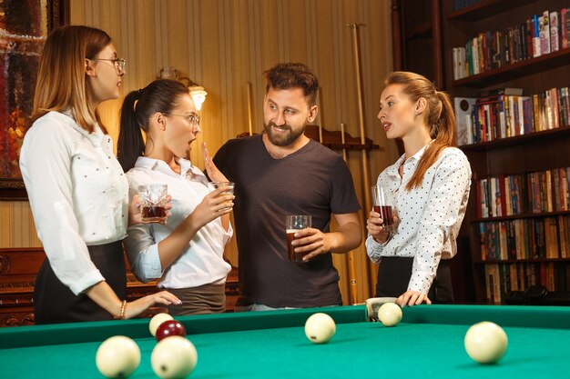 Jovens sorrindo, homens e mulheres jogando bilhar no escritório ou em casa, depois do trabalho.