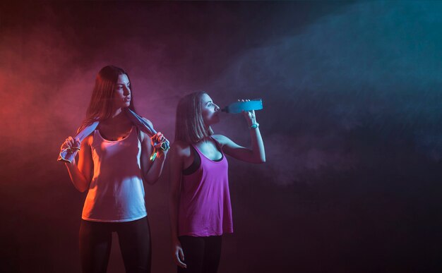 Jovens sportswomen descansando no estúdio escuro