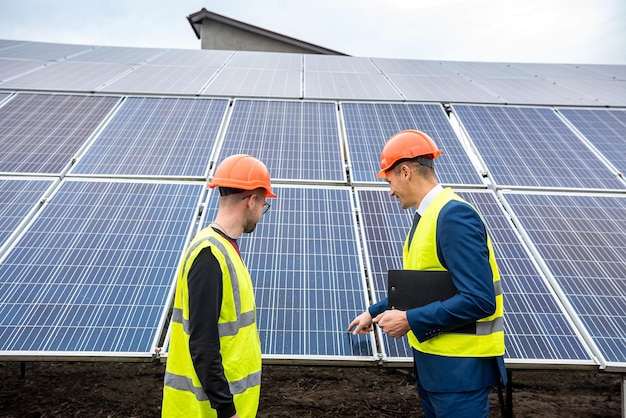 Jovens trabalhadores em capacetes de jaquetas de trabalho discutem o plano de trabalho de painéis solares para economia de energia elétrica. conceito de eletricidade verde