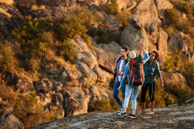 Jovens viajantes com mochilas sorrindo, dando highfive, andando no canyon