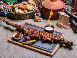 Foto grátis kebab de carne de vista lateral no espeto com batatas grelhadas e legumes com molho e fogo em uma placa