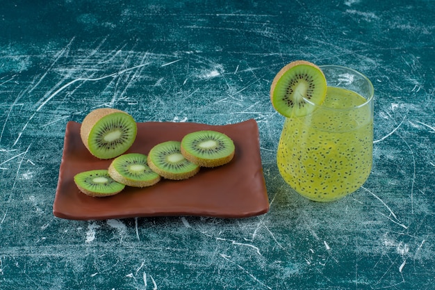 Foto grátis kiwi fatiado em um prato marrom ao lado de um copo de suco de kiwi, na mesa de mármore.