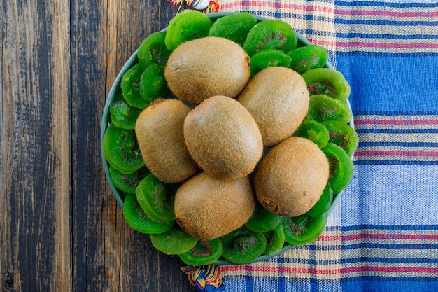 Kiwi fresco em um prato com kiwi seco plano deitado sobre fundo de madeira e pano de piquenique