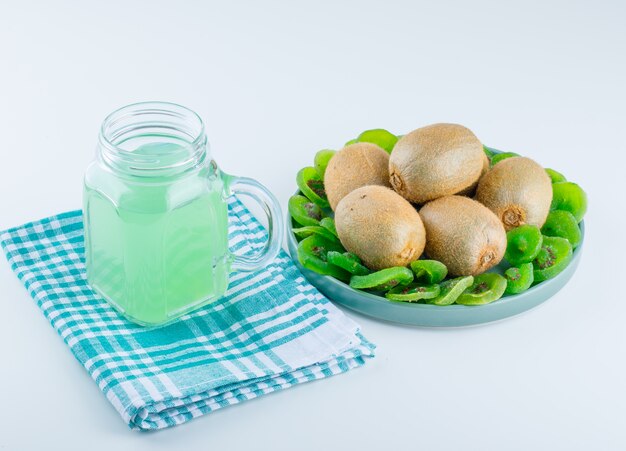 Kiwi fresco em um prato com kiwi seco, vista de alto ângulo na toalha de piquenique e fundo branco