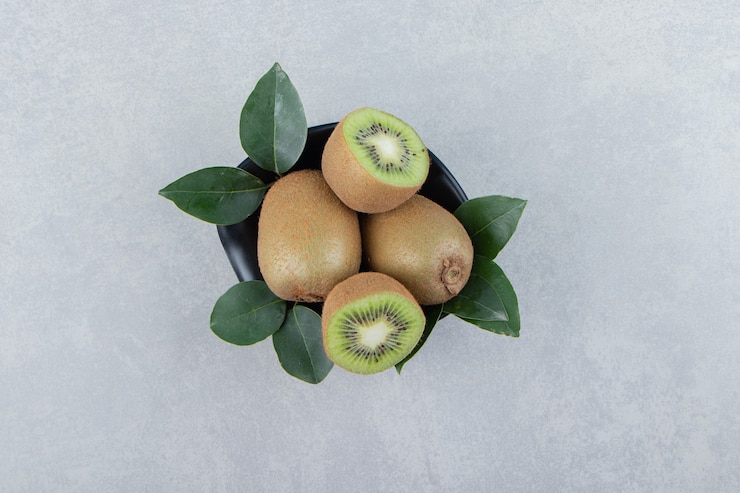 Foto grátis kiwis inteiros e fatiados em uma tigela preta.