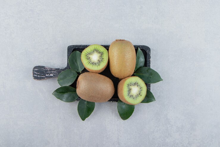 Foto grátis kiwis inteiros e fatiados na tábua de corte preta