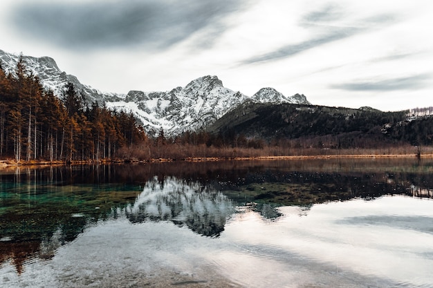 Lago perto de montanha coberta de neve sob céu nublado durante o dia