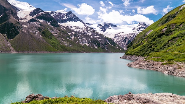 Lago Stausee Mooserboden cercado por montanhas sob a luz do sol em Kaprun, Áustria