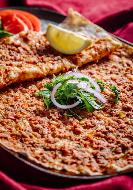 Lahmacun com recheio de carne servido com cebola picada, salsa, tomate e limão.