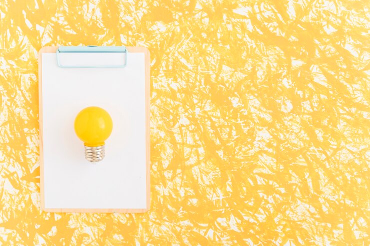 Foto grátis lâmpada amarela em papel branco sobre a área de transferência contra pano de fundo amarelo