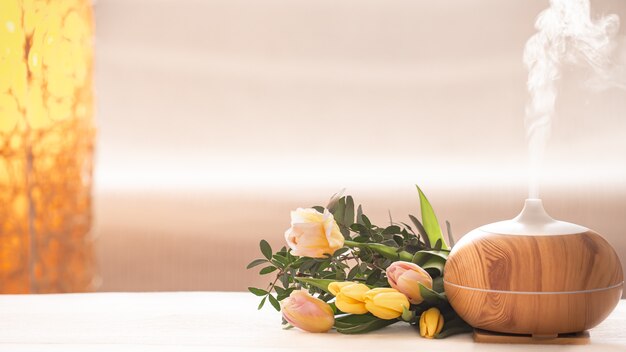 Lâmpada difusor de óleo de aroma em cima da mesa em um fundo desfocado com um lindo buquê de tulipas primavera.