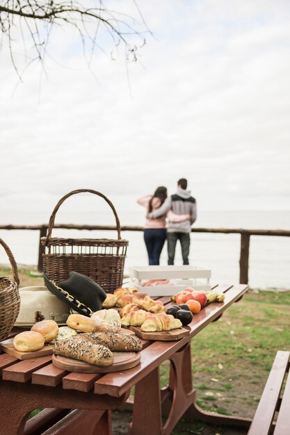 Lanche e frutas na mesa de piquenique com casal no fundo com vista para o mar