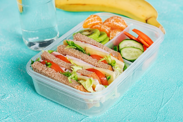 Lancheira escolar com sanduíche, legumes, água e frutas na mesa.
