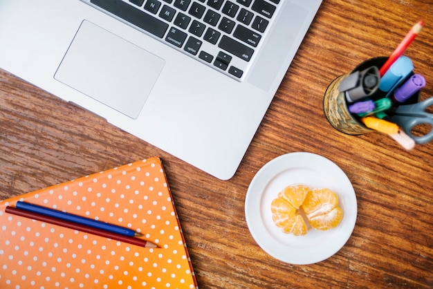 Foto grátis lápis; caderno; laptop e laranja na mesa de madeira