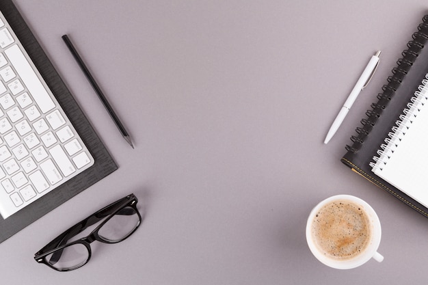 Lápis, caneta e notebooks perto de teclado, óculos e copo