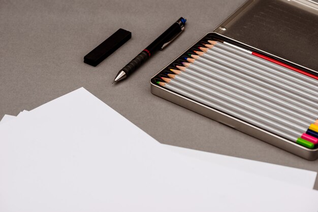 Lápis coloridos, caneta, papel na mesa cinza