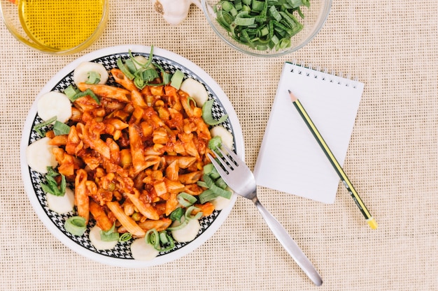 Lápis e caderno perto de macarrão