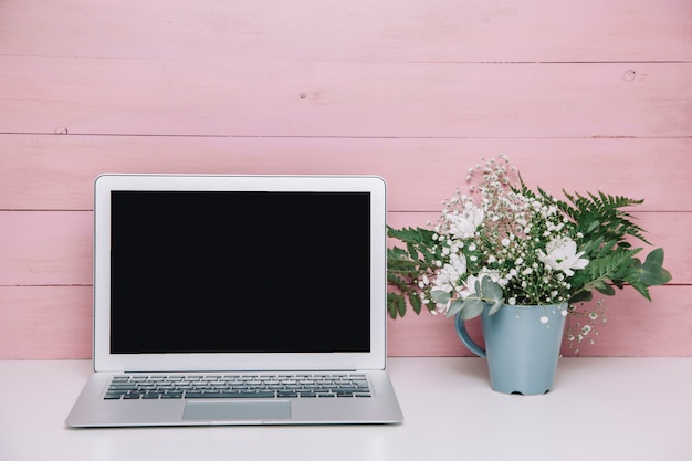 Laptop ao lado do vaso de flores