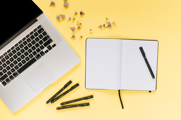 Laptop com canetas de feltro; caderno em branco com flores de lavanda em fundo amarelo