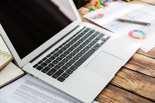 Laptop com gráficos de pizza ao lado dele e de outros papéis