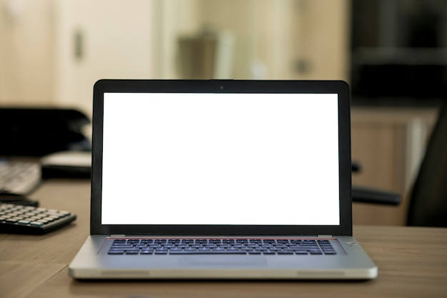 Laptop com tela branca em branco sobre a mesa de madeira