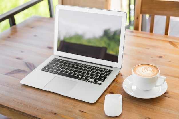 Laptop com tela em branco em uma mesa de madeira e uma chávena de café