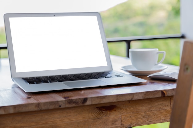 Laptop com tela em branco em uma mesa de madeira e uma chávena de café