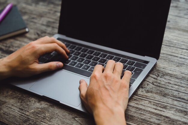 laptop em uma mesa de madeira, mãos de um homem que trabalha em um computador